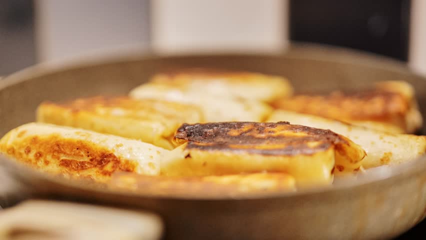 Close up of stuffed pancakes frying in pan with golden crust in warm kitchen