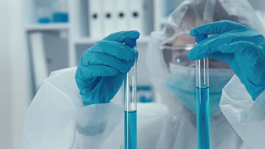 In a sterile lab, a focused scientist in protective gear examines test tubes with vibrant blue solutions, demonstrating exceptional precision and attention to detail during critical experiments