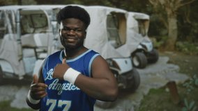 Man with thumbs up and finger pointing gesture in forest near parked golfcarts wearing blue los angeles jersey; playful confidence. - Powered by Shutterstock - Get 15% off with code: PIKWIZARD15
