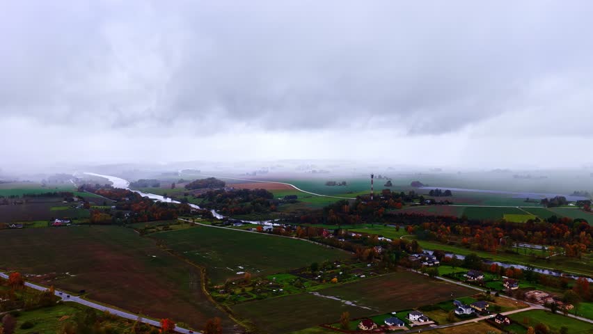 River winding through rural farmland countryside with autumn trees under cloudy sky