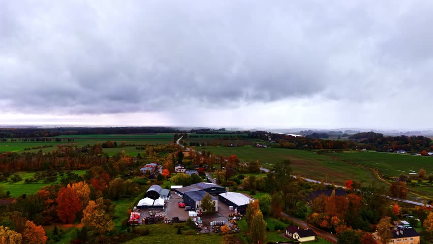 Aerial of vibrant autumn rural landscape under overcast sky, with buildings a road