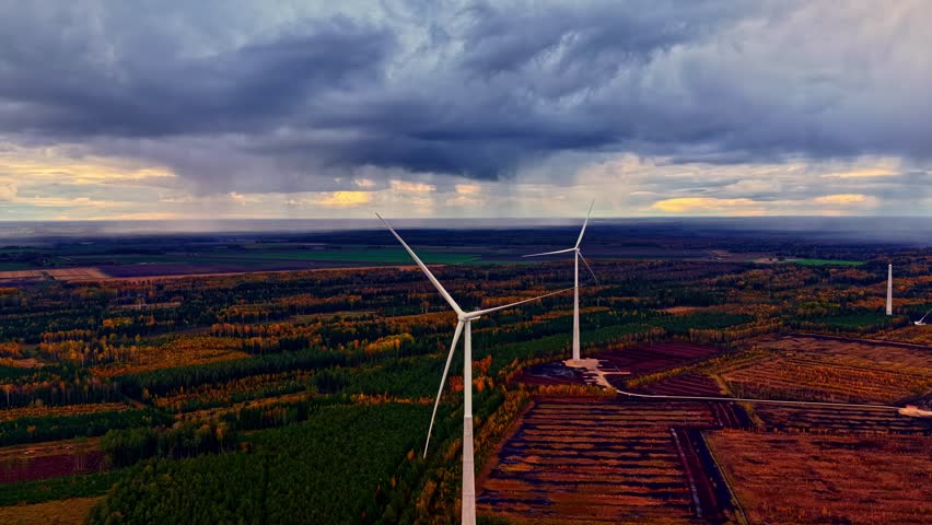Aerial of wind turbines and vibrant autumn farmland landscape with dramatic, moody sky