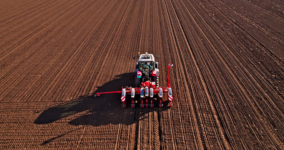 Tractor planting seeds in a vast plowed field under a cloudy sky
