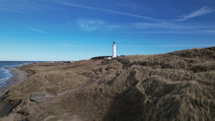 Scenic view of Hirtshals Lighthouse standing above green dunes under a clear blue sky on a warm summer day in northern Denmark.