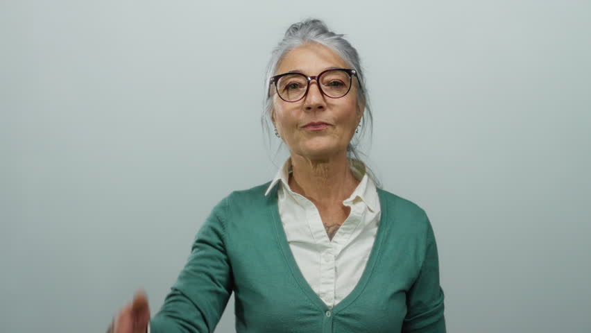Senior woman with grey hair covering her eyes playfully stands against an isolated white background, wearing a white shirt and green sweater, conveying a lighthearted mood.