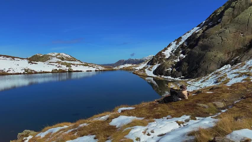 Man Resting by Alpine Lake.
Hiker lying on golden grass watching snowy peaks and crystal water below.