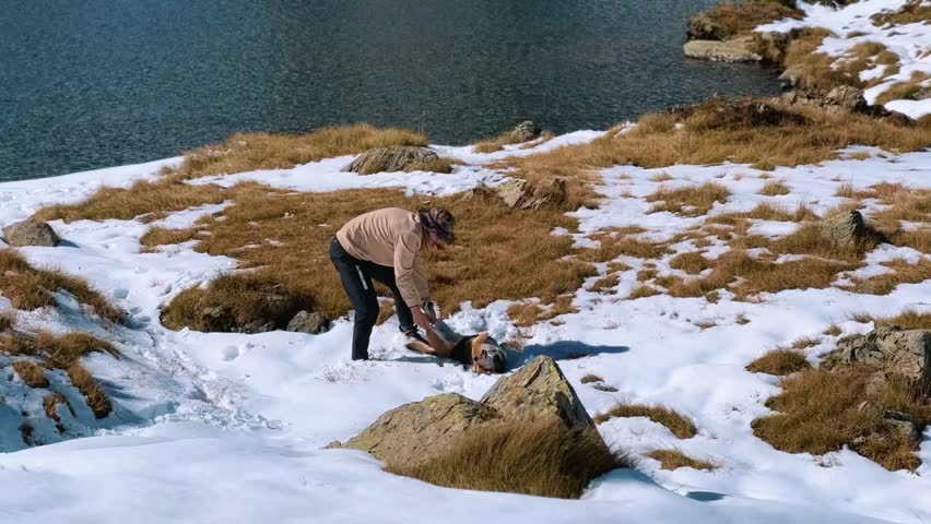 Man Enjoying Snowy Adventure.
Traveler smiling and playing with dog surrounded by snow and peaks.
