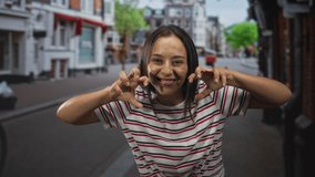 Woman showing hands in a claw gesture while laughing and leaning forward on a cobbled street with storefronts and a bicycle behind her; joy youthful play. - Powered by Shutterstock - Get 15% off with code: PIKWIZARD15