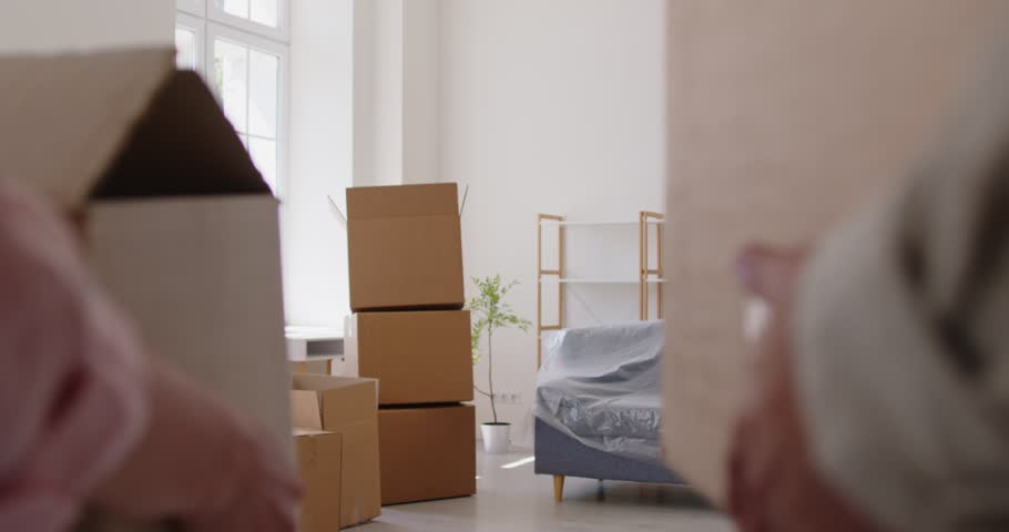Smiling couple carry cardboard boxes while moving into new home apartment. Happy people enjoying success start of family life, cooperation in unpacking, planning furniture and decoration with optimism
