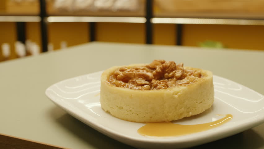 Close-up of a delicious caramel walnut tart served on a white plate. Handmade dessert with a golden, shiny texture.
