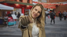 Woman smiling on urban street under lanterns extends fist playfully towards camera surrounded by blurred people and red market tents. - Powered by Shutterstock - Get 15% off with code: PIKWIZARD15