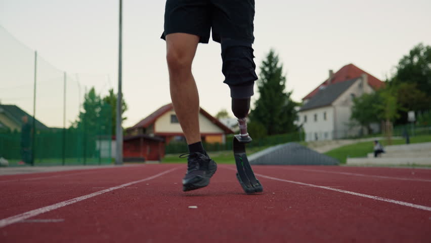 Determined athlete using a prosthetic running leg, a blade with a heel plate to jump on the track, close up. Strength, agility, and motivation concepts.