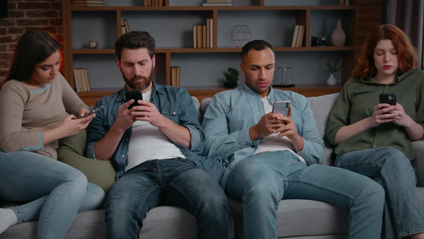 Focused four diverse friends overuse mobile phones addiction internet social media dependence relaxing at home boring party looking in smartphones addicted multiethnic men women ignoring each other
