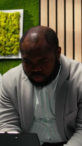Vertical Video African american anxious male candidate reading his speech sitting in queue in the hallway, presenting his qualifications on the CV. Preparing for the selection and hiring process