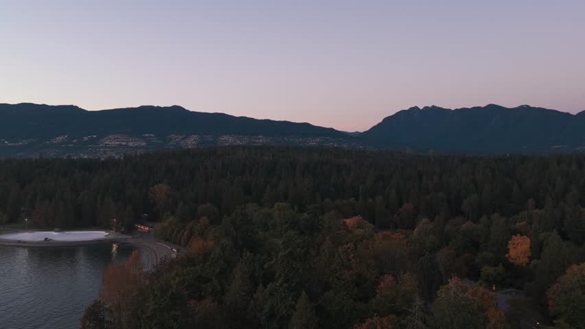 Aerial wide reverse pullback shot of Stanley Park at magic hour in Vancouver, British Columbia, Canada. 4K