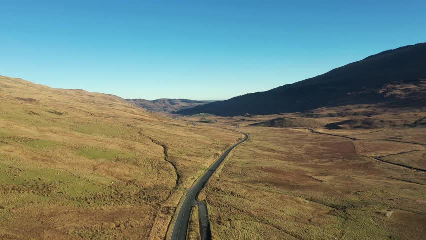 Aerial view of cars on a countryside road through an ample desolate valley in Wales area of Snowdonia with concepts of travel and transportation