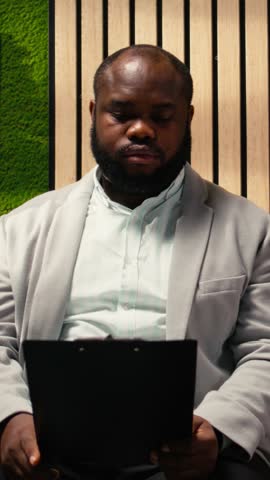 Vertical Video Professional diverse candidates awaiting start of job interview, showcasing anticipation in office hallway, preparing with information for the recruitment process. Career opportunity