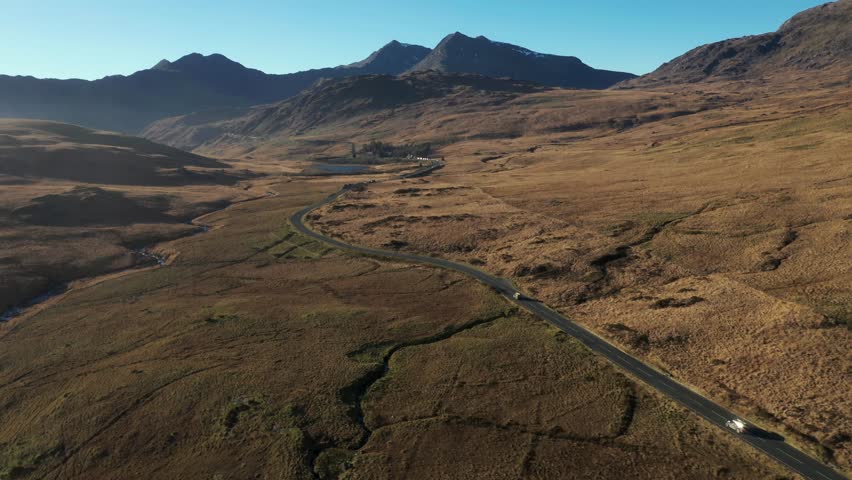 Aerial view of cars on a countryside road through an ample desolate valley in Wales area of Snowdonia with concepts of travel and transportation