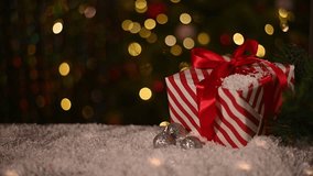 red and white striped Christmas gift with red ribbon sits next to silver disco ball ornaments on snowy surface. background soft bokeh lights from Christmas tree, adding festive touch. - Powered by Shutterstock - Get 15% off with code: PIKWIZARD15
