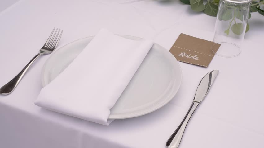 A beautifully arranged place setting for the bride, featuring a white napkin on a clean plate and a stylish name card. Simple yet elegant details enhance the decor.