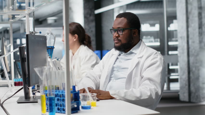 Jolly laboratory researcher using computer monitor, processing DNA patient data for clinical research. Joyous african american lab employee looking at analysis diagnostics on PC - Powered by Shutterstock - Get 15% off with code: PIKWIZARD15