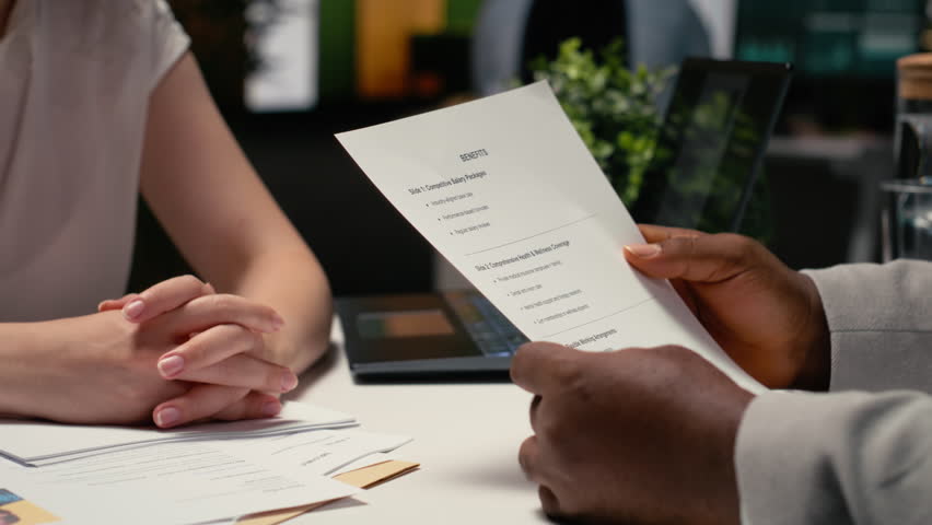 Close up of candidate going over benefits package and salary options, meeting with a recruiter to discuss the monthly perks for health and wellness insurance within contract deal. Camera B.