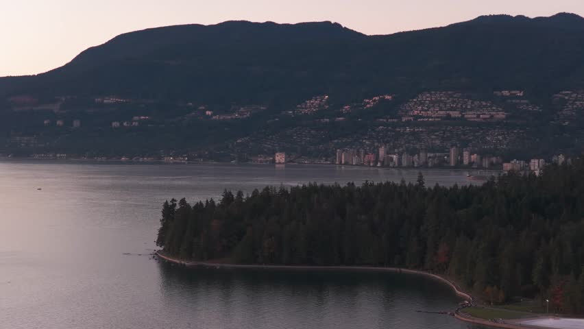 Aerial telephoto panning shot of Stanley Park towards West Vancouver during sunset in British Columbia, Canada. 4K