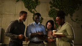 Multinational team of colleagues having a coffee break and discussing a project on a digital tablet in a modern eco friendly office lobby - Powered by Shutterstock - Get 15% off with code: PIKWIZARD15