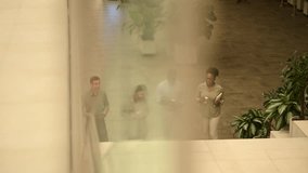 High angle view of a diverse group of four professional colleagues walking up the stairs, holding coffee cups and talking in a modern office building - Powered by Shutterstock - Get 15% off with code: PIKWIZARD15