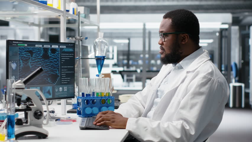 High tech lab technician at desk typing on PC keyboard, looking at molecular model, doing research tasks. African american man using bioengineering program on PC in medical lab, camera B - Powered by Shutterstock - Get 15% off with code: PIKWIZARD15