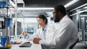 Multiracial lab engineers inspect liquids in test tube, looking for breakthroughs during clinical trials. Asian and African american men comparing chemicals vials, testing formula, camera A - Powered by Shutterstock - Get 15% off with code: PIKWIZARD15