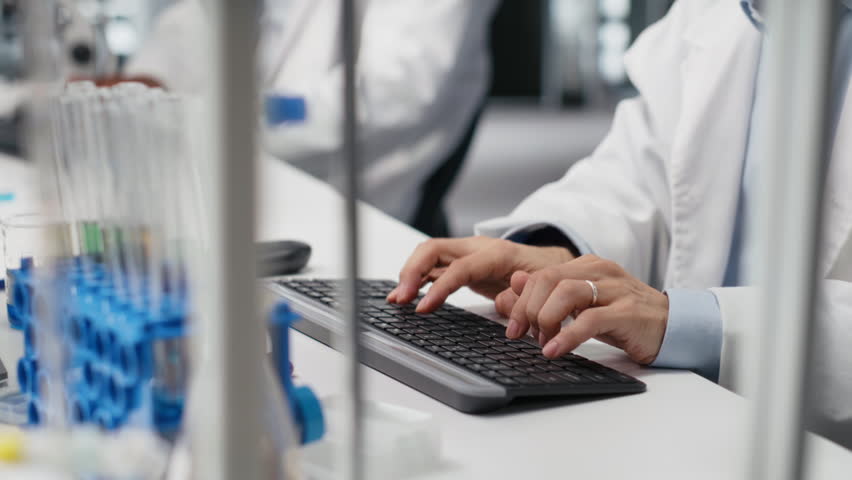 Lab professional examines test tube sample under controlled lighting for transparency and consistency. Scientist uses lamp illumination to observe liquid properties and detect impurities, camera B