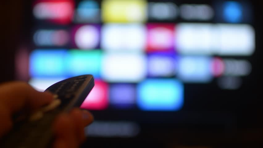 Person browses smart TV menu using remote control, switching between streaming services and selecting content to watch