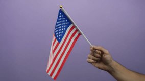 Man holding an american flag against a purple background, representing patriotism and national pride in a simple isolated setting. - Powered by Shutterstock - Get 15% off with code: PIKWIZARD15