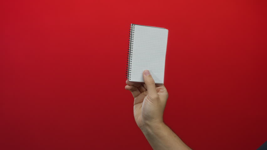 Caucasian man's hand holding a small notebook against a solid red wall background, highlighting simplicity and minimalism in an isolated setting. - Powered by Shutterstock - Get 15% off with code: PIKWIZARD15