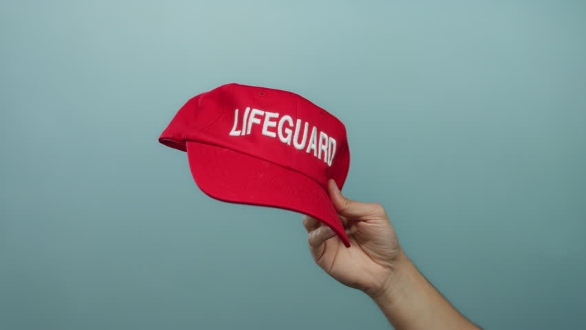 Man holding red lifeguard cap against blue wall showcasing safety and aquatic theme.