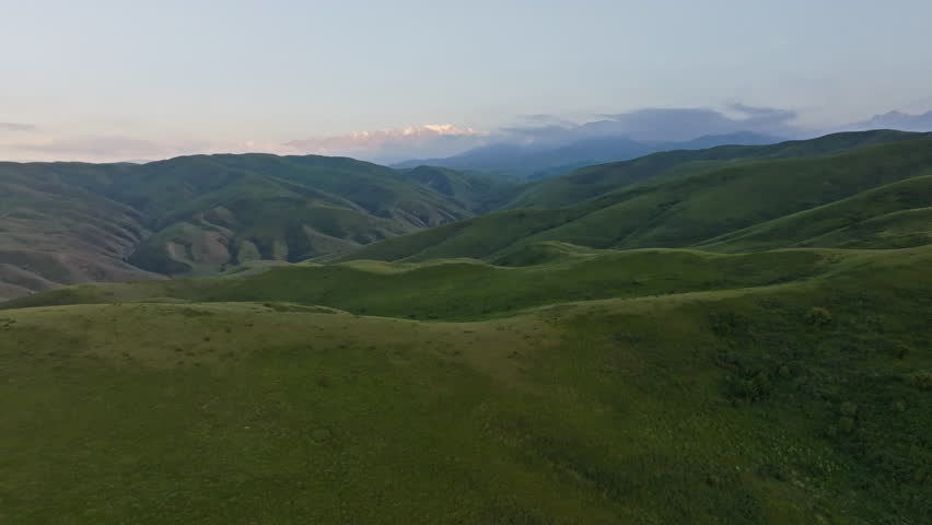 Serene mountains and hills under a dusk sky in evening Kyrgyzstan. Drone view with dolly forward camera movement.