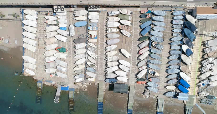 Drone starting seaward, revealing HUD overlay while boats launching and aligning, mapping moorings. Marina, docks, vessels, aerial, coastal, sunlit, reflections