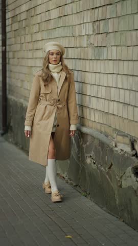 Elegant woman in beige trench coat walking down the street. Concept of woman in autumn clothes.
