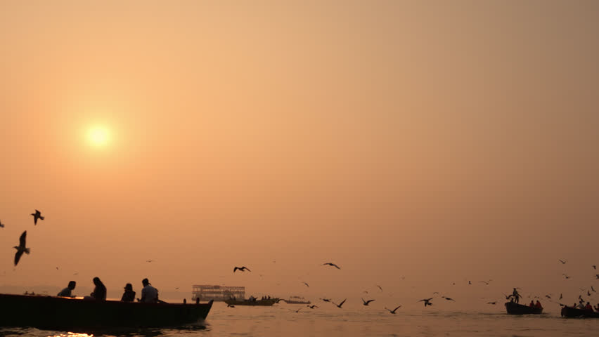 A group of people rides a wooden boat on the Ganga River in Banaras during golden sunrise