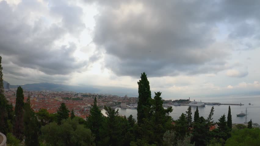 Panoramic view of Split, Croatia, with dramatic clouds over the old town and harbor. Cruise ships anchored near the coastline, scenic cityscape and Adriatic Sea.