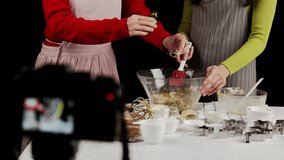 Close-up of hands adding liquid flavor extract into cookie dough mix in glass bowl during baking video shoot, surrounded by utensils, cookie cutters, and filming gear - Powered by Shutterstock - Get 15% off with code: PIKWIZARD15