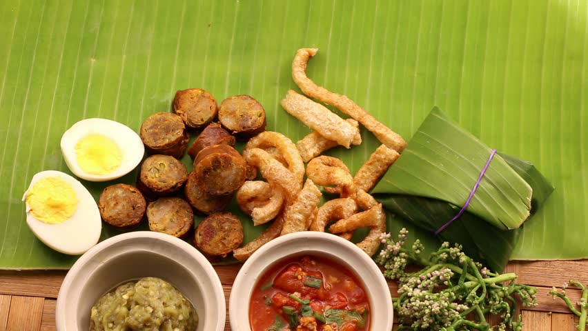 A set of traditional Northern Thai food, Known as Lanna cuisine, featuring the iconic spicy herbal pork sausage (Sai Oua), two chili dips (Nam Prik Noom and Nam Prik Ong) and crispy fried pork skin.