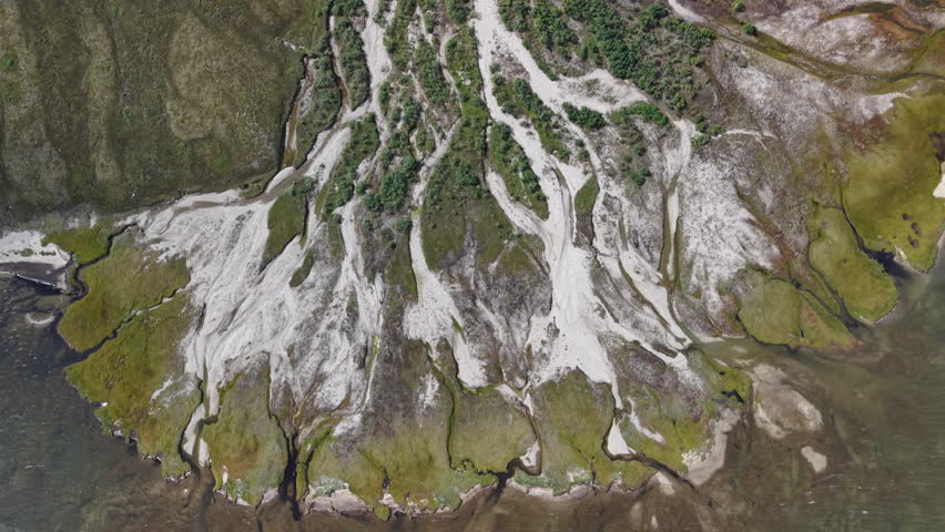 Topdown drift over white sand gullies and grassy edges at the tide line. Streams slice through permafrost slopes and meet cold water under soft clouds. Location Lavrentiya Bay, Chukotka, Russia