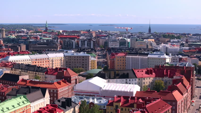 Helsinki, Finland, showcases its iconic red rooftops from above. The Baltic Sea and various landmarks stretch into the distance on a bright, sunny day
