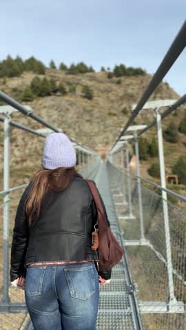 Woman wearing a purple coat and hat walking across the Pont Tibetà bridge in Canillo, Andorra. Andorra Tourism.
