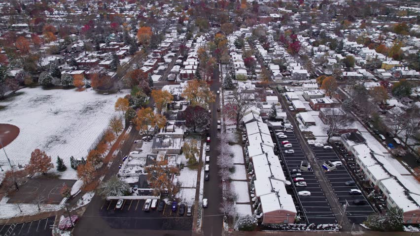 Drone shot and aerial view of Columbus, Ohio neighborhood homes, buildings, roads, buildings, and businesses during late fall after winter snowfall snow falling and colorful autumn trees and leaves up
