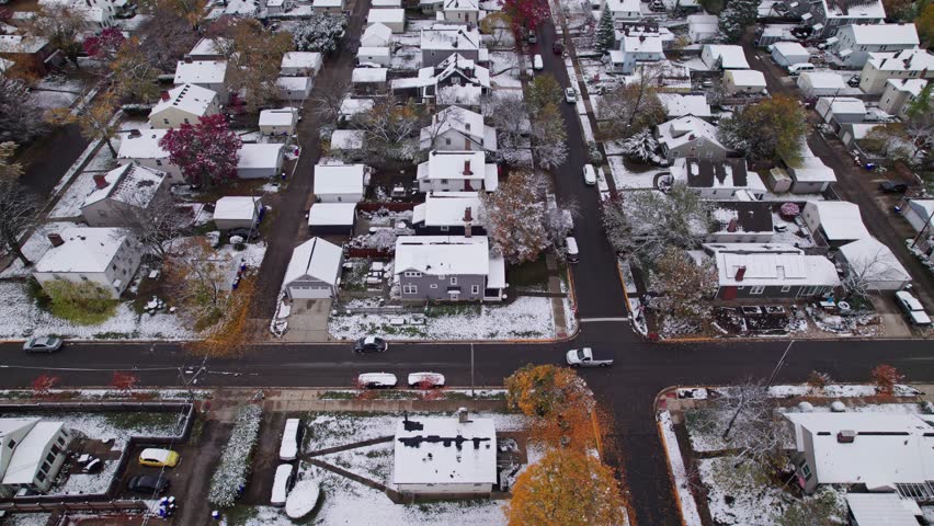 Drone shot and aerial view of Columbus, Ohio neighborhood homes, buildings, roads, buildings, and businesses during late fall after winter snowfall snow falling and colorful autumn trees and leaves up