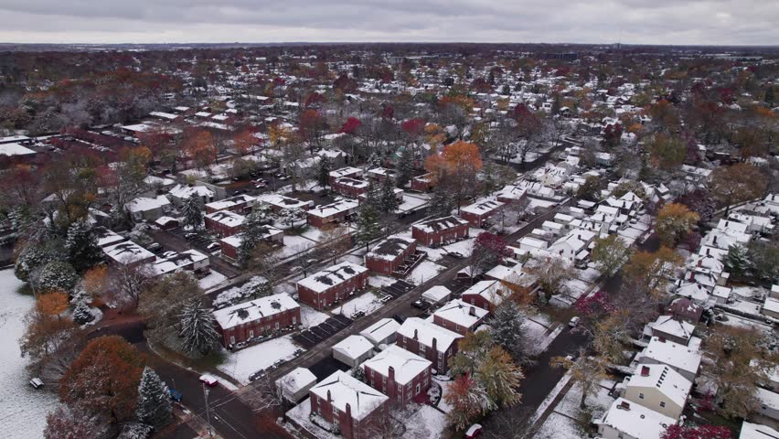 Drone shot and aerial view of Columbus, Ohio neighborhood homes, buildings, roads, buildings, and businesses during late fall after winter snowfall snow falling and colorful autumn trees and leaves up