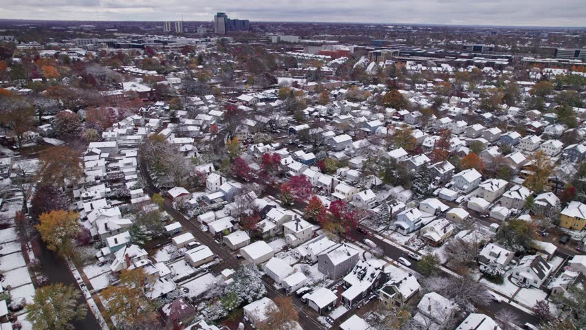 Drone shot and aerial view of Columbus, Ohio neighborhood homes, buildings, roads, buildings, and businesses during late fall after winter snowfall snow falling and colorful autumn trees and leaves up